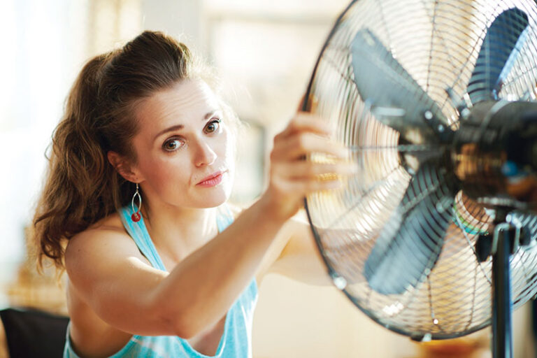 Woman adjusting a standing fan for better cooling at home