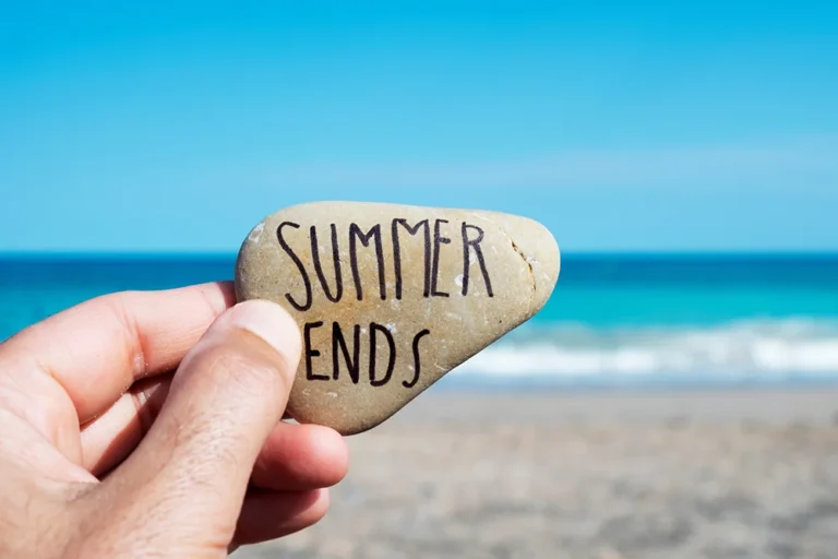 Hand holding stone with 'Summer Ends' near beach and ocean background